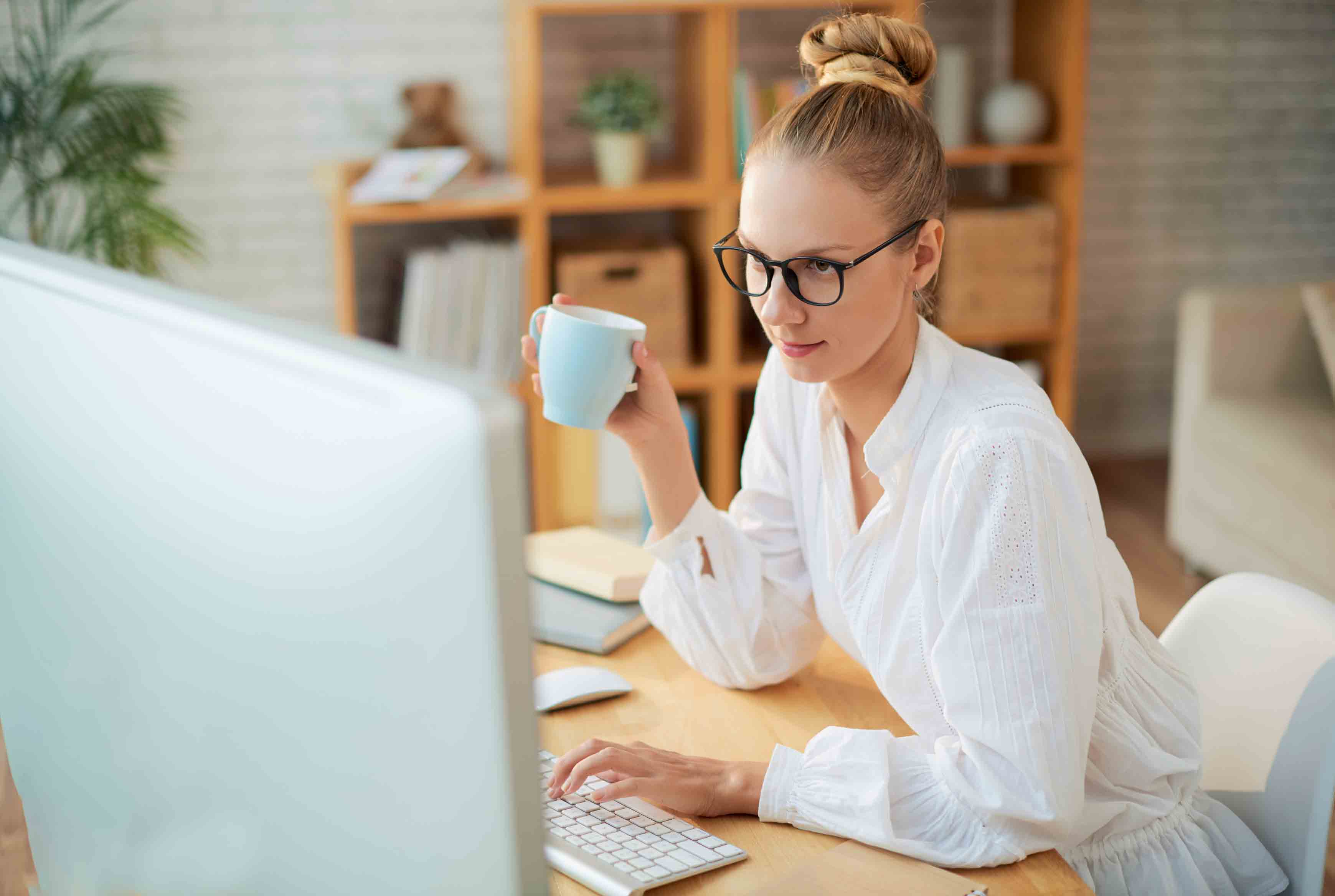 young woman working on Mac, drinking coffee
