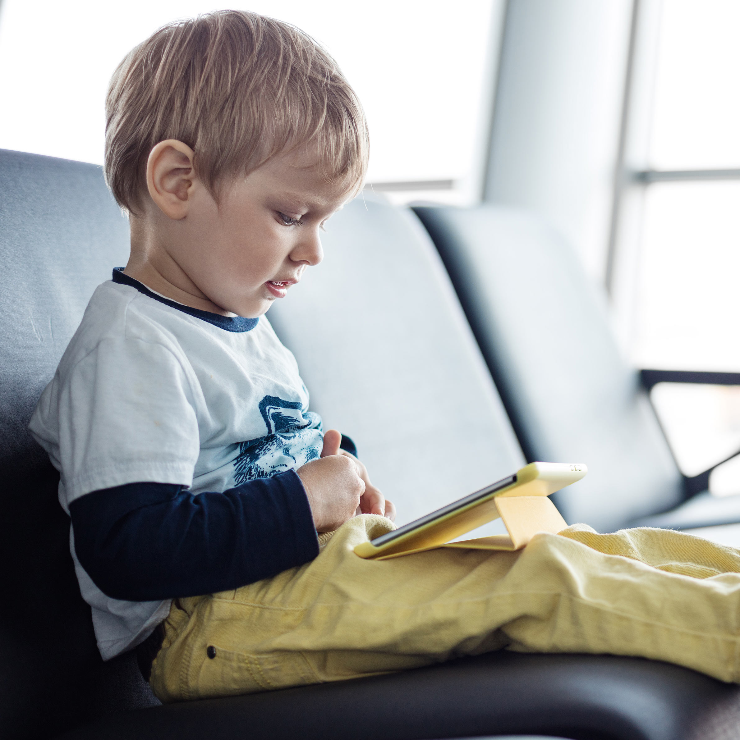 Little boy sitting in an airport departure hall and using his tablet
