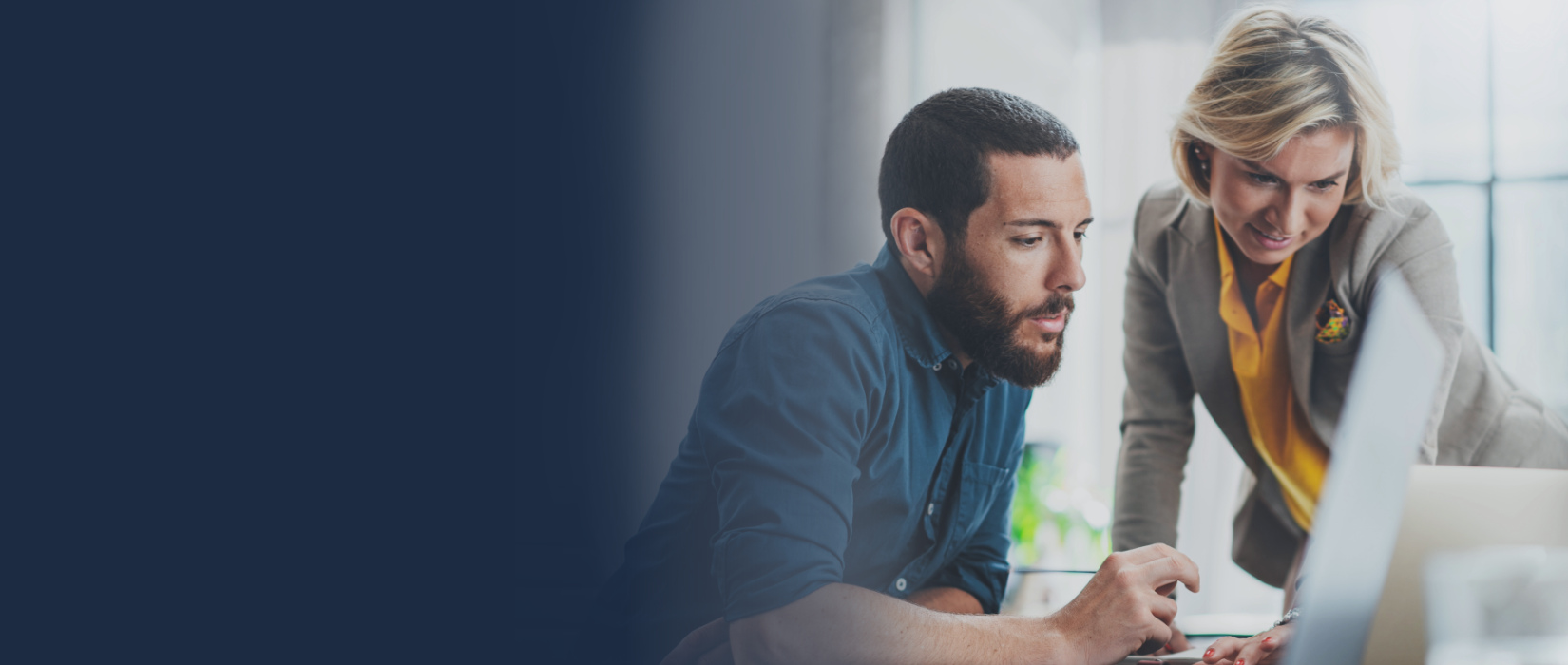 Man working on a computer while a woman looks at the screen and collaborates beside him.